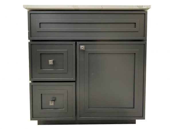 Dark gray bathroom vanity with light marble countertop, horizontal drawer at top, two stacked drawers on left side, and one large cabinet door on right, all with square nickel hardware