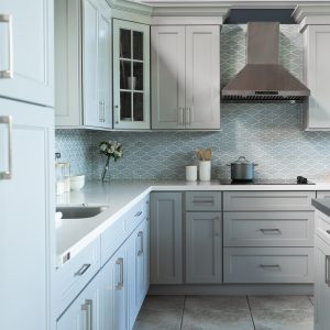 M22 - 2 Light blue and white kitchen with quatrefoil tile backsplash, dark range hood, and shaker-style cabinets with dark countertops