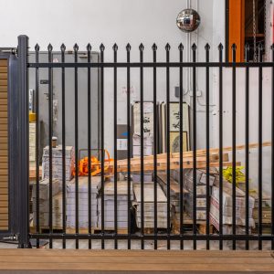 Black metal vertical bar fence gate with spear points installed in front of wooden garage doors at a residential property