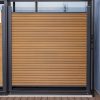 Modern composite deck gate with horizontal wood slat panels and dark metal frame on wooden deck with ocean view