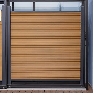 Modern composite deck gate with horizontal wood slat panels and dark metal frame on wooden deck with ocean view