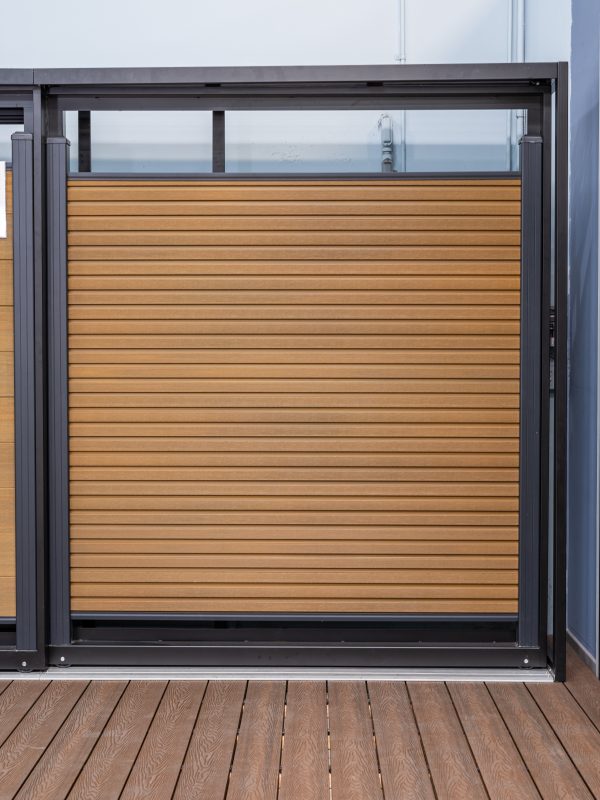 Modern composite deck gate with horizontal wood slat panels and dark metal frame on wooden deck with ocean view