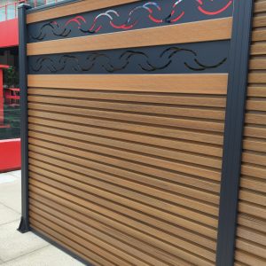 Composite wooden fence with horizontal slats and decorative metal wave inserts in dark and red colors