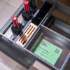 Close-up overhead view of kitchen drawer organizer with wine bottles, wooden utensil holder, and green product information card