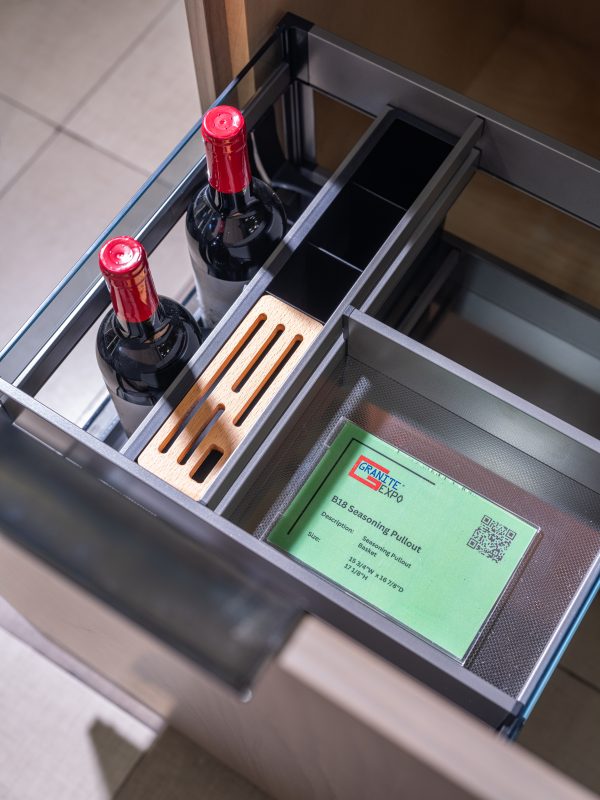 Close-up overhead view of kitchen drawer organizer with wine bottles, wooden utensil holder, and green product information card