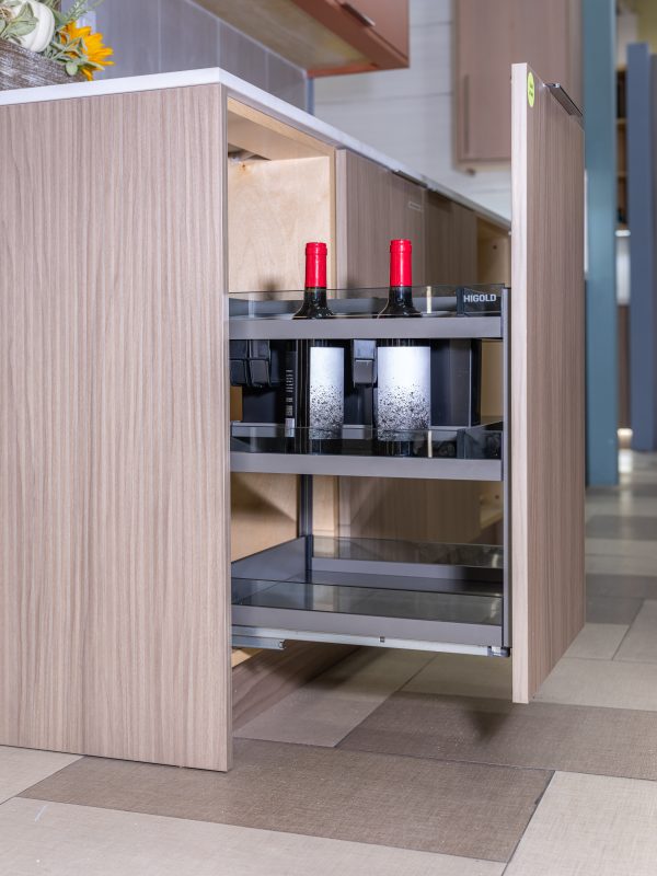 Modern kitchen island detail showing open cabinet with HIGOLD coffee machine, red candles, and wooden accessories inside