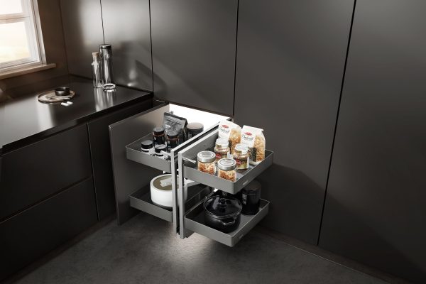 Pull-out kitchen cabinet organizer with multiple tiers storing jars, pasta boxes, and cookware in a modern black kitchen