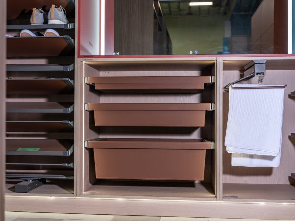 Modern closet storage system with light wood frame, multiple brown pull-out drawers, open shelving with folded items on left, and white towel rack on right side