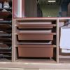 Modern closet storage system with light wood frame, multiple brown pull-out drawers, open shelving with folded items on left, and white towel rack on right side