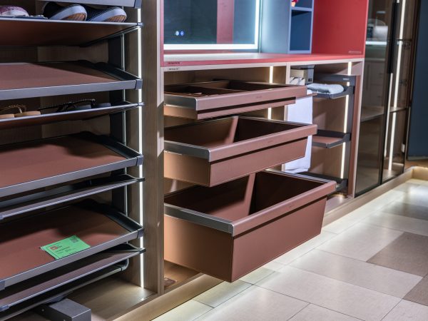 Angled view of closet interior showing extended brown drawers, open shelving with organized items, and mirrored doors on right side with warm LED lighting