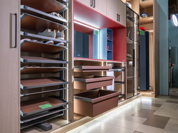 Wide angle view of a luxury walk-in closet with brown pull-out drawers, multiple shelving units, red accent wall with mirror, and LED lighting throughout