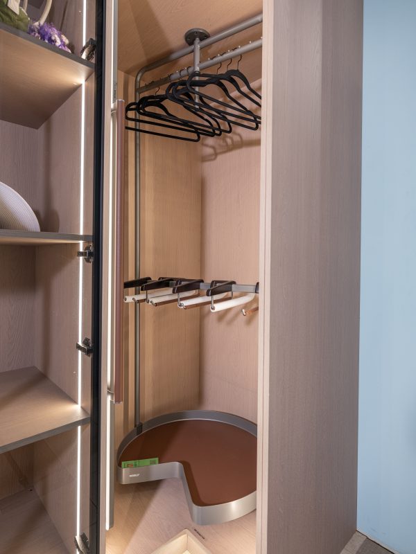 Walk-in closet interior showing brown pull-out drawers, metal hanging rod with black hangers, and multiple shelves with accent lighting