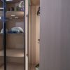 Minimalist closet with glass sliding doors, wooden shelving, LED lighting, and neatly folded clothing and accessories