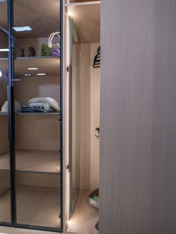 Minimalist closet with glass sliding doors, wooden shelving, LED lighting, and neatly folded clothing and accessories