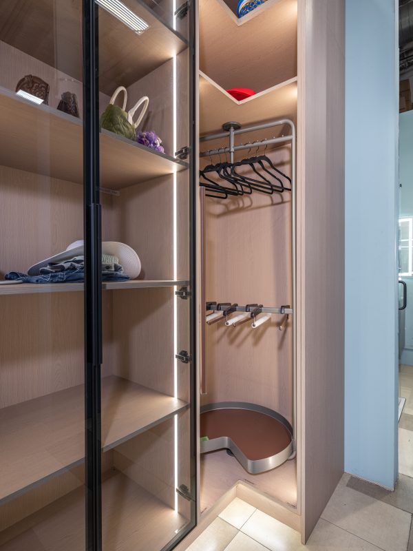 Open walk-in closet displaying hanging rod with black hangers, white item on shelf, and brown storage container