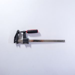 Heavy-duty bar clamp with black metal screw mechanism, red and black grip handle, and extended steel bar on white background