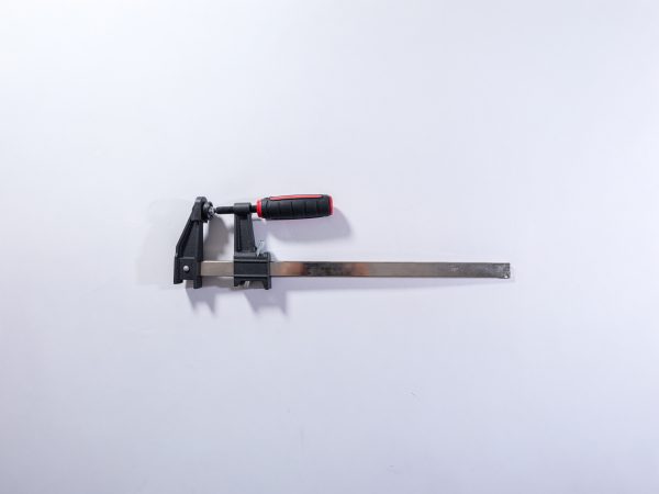 Heavy-duty bar clamp with black metal screw mechanism, red and black grip handle, and extended steel bar on white background