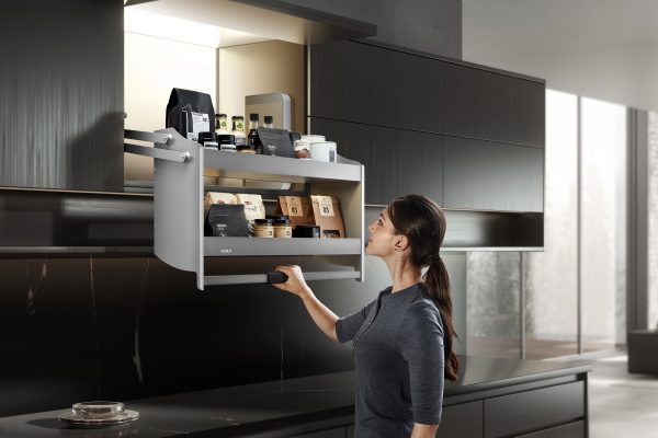 Woman opening a wall-mounted pull-out kitchen storage drawer with organized coffee and kitchen items