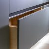 Close-up of stainless steel and black modern handle integrated into gray cabinet drawer with wooden interior visible
