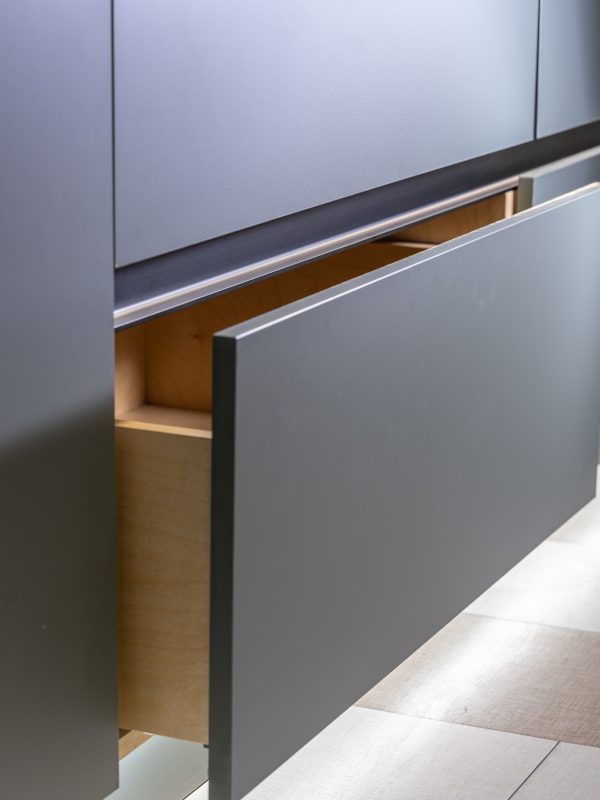 Close-up of stainless steel and black modern handle integrated into gray cabinet drawer with wooden interior visible