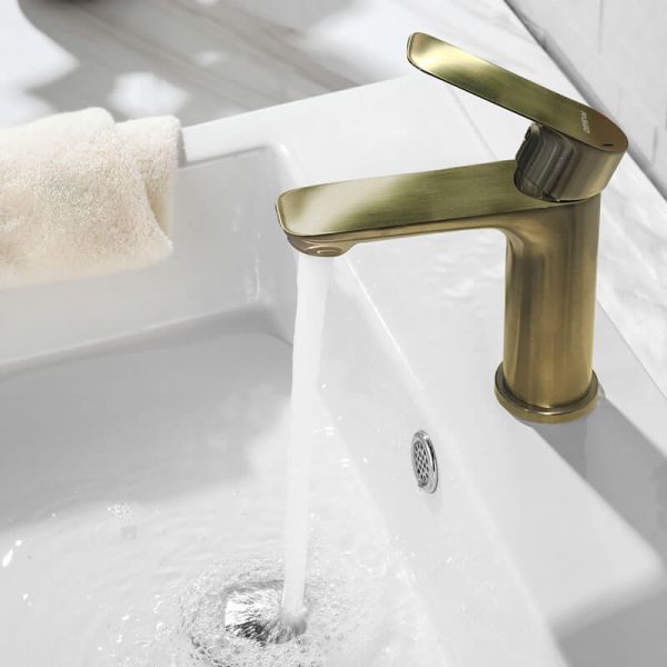 Gold brushed brass bathroom faucet with single lever handle and curved spout installed on white bathroom sink