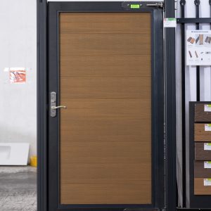 Modern black aluminum framed gate with horizontal wood grain door panel in golden oak finish displayed in showroom