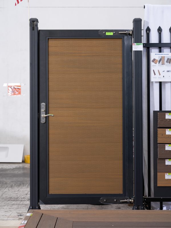 fence_6 Modern black aluminum framed gate with horizontal wood grain door panel in golden oak finish displayed in showroom