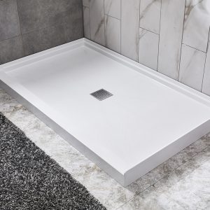 White rectangular shower base with center drain on marble tile bathroom floor next to dark area rug