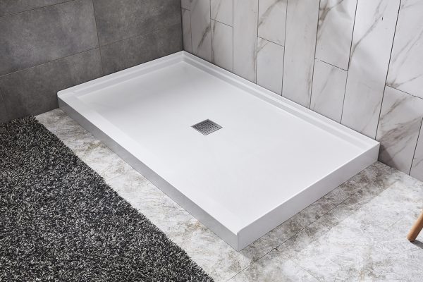 White rectangular shower base with center drain on marble tile bathroom floor next to dark area rug