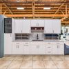 White kitchen cabinet display with closed cabinet doors, gray countertop, open shelf units, and integrated sink in warehouse setting