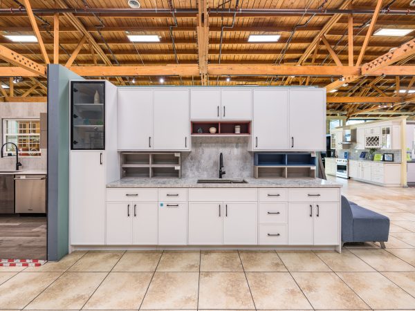 White kitchen cabinet display with closed cabinet doors, gray countertop, open shelf units, and integrated sink in warehouse setting