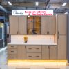 Modern light wood European cabinet display with white countertop, glass-front upper cabinets, closed lower cabinets, and yellow accent lighting in showroom