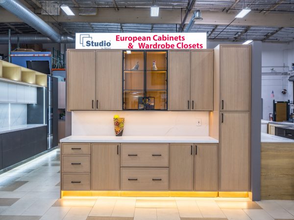 Modern light wood European cabinet display with white countertop, glass-front upper cabinets, closed lower cabinets, and yellow accent lighting in showroom