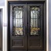 Ornate black double entry doors with decorative wrought iron scrollwork and glass panels in white frame