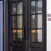 Black double doors with 6-pane grid windows showing weathered wood and stone textures with warm orange and gold tones