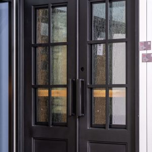 Black double doors with 6-pane grid windows showing weathered wood and stone textures with warm orange and gold tones