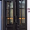 Black double doors with 6-pane grid windows displaying textured glass and wood grain patterns with golden accents