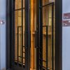 Black double doors with 8-pane grid windows and golden textured glass panels, illuminated from interior with warm lighting
