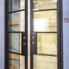 Black framed double doors with clear glass panes and gold hardware, one door open showing interior