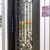 Black metal entry door with elaborate wrought iron filigree design and cream frame
