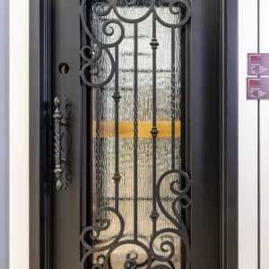 Black wrought iron decorative entry door with ornate scrollwork and weathered wood insert