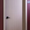 Closed light wood interior door with minimalist design and black handle against burgundy wall