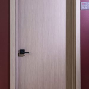 Closed light wood interior door with minimalist design and black handle against burgundy wall