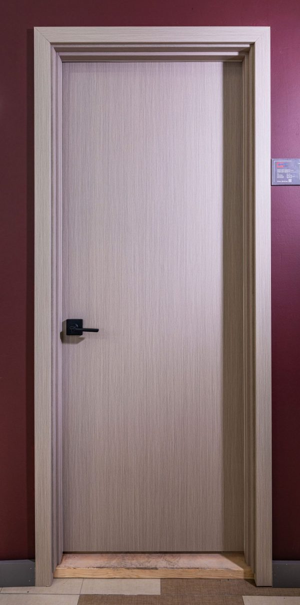Closed light wood interior door with minimalist design and black handle against burgundy wall