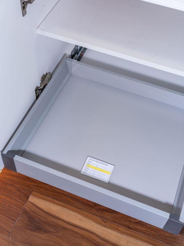 Close-up view of a pull-out drawer mechanism inside a white kitchen cabinet with a yellow installation label visible
