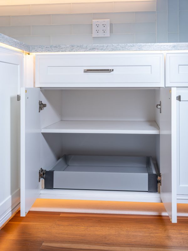White kitchen cabinet with open doors revealing two pull-out drawers with soft-close hardware and gray interior