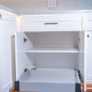 White kitchen cabinet interior with gray pull-out drawer trays and white subway tile backsplash above countertop