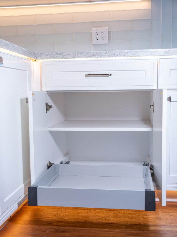 White kitchen cabinet interior with gray pull-out drawer trays and white subway tile backsplash above countertop