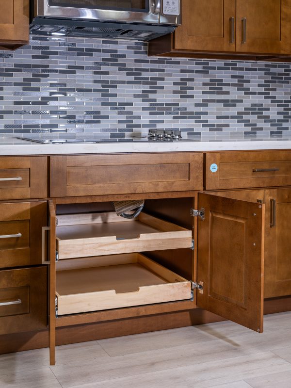 Open kitchen cabinet with wooden drawers and stainless steel microwave mounted above gray tiled backsplash