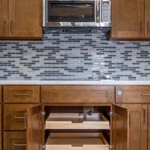 Kitchen cabinet with stainless steel microwave, gray subway tile backsplash, and open wooden drawers below
